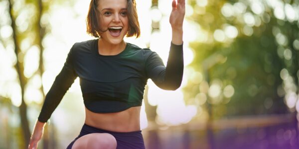 Emotional happy woman in black sport clothing training on fresh air during warm day. Attractive female with brown hair having morning workout at park.